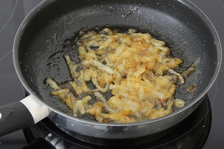 Agregar la miel a la cebolla para hacer las empanadillas de sobrasada y queso