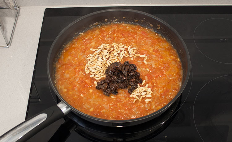 Añadir los tomates, el vino, las pasas y los piñones. Cocinar hasta obtener una salsa