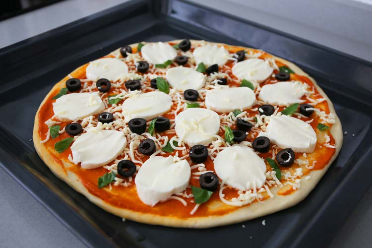 Pizza casera con tomate, queso mozzarella y aceitunas antes de meterla en el horno