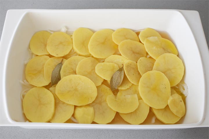 Patatas, cebolla y laurel listos en una fuente para hornear
