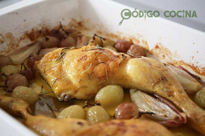 Pollo de aspecto dorado y crujiente acompañado de uvas y chalotas