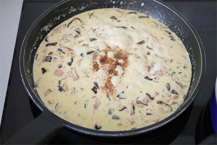 Salsa cremosa de nata con setas y jamón cocido cocinándose en una sartén